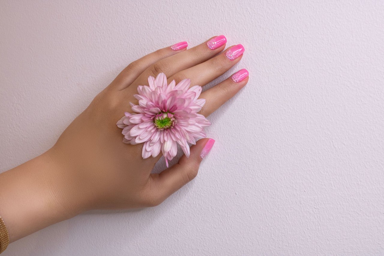 ピンクの花を手にのせた、ピンクのネイルの手元